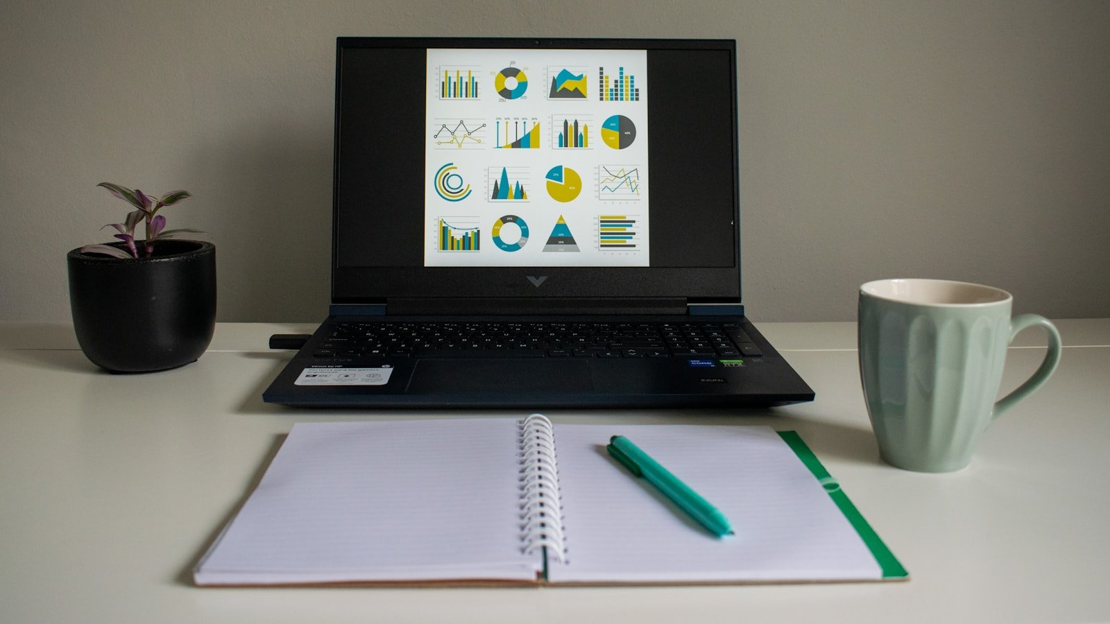Como Fazer Planilha Financeira em 20 Minutos do Zero Laptop com gráficos ao lado de caderno usado para fazer a planilha financeira