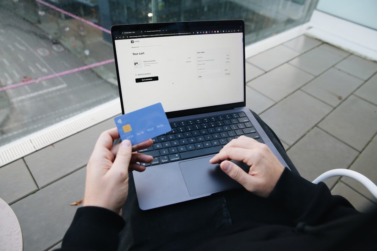 Pessoa conferindo o débito automático no notebook com o cartão na mão