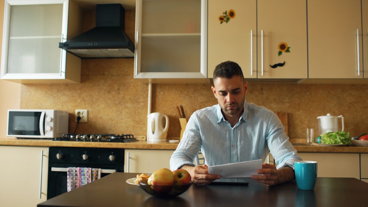 Débito Automático: Como Cancelar em 2 Dias Úteis Homem conferindo as cobranças em débito automático da conta na mesa da cozinha