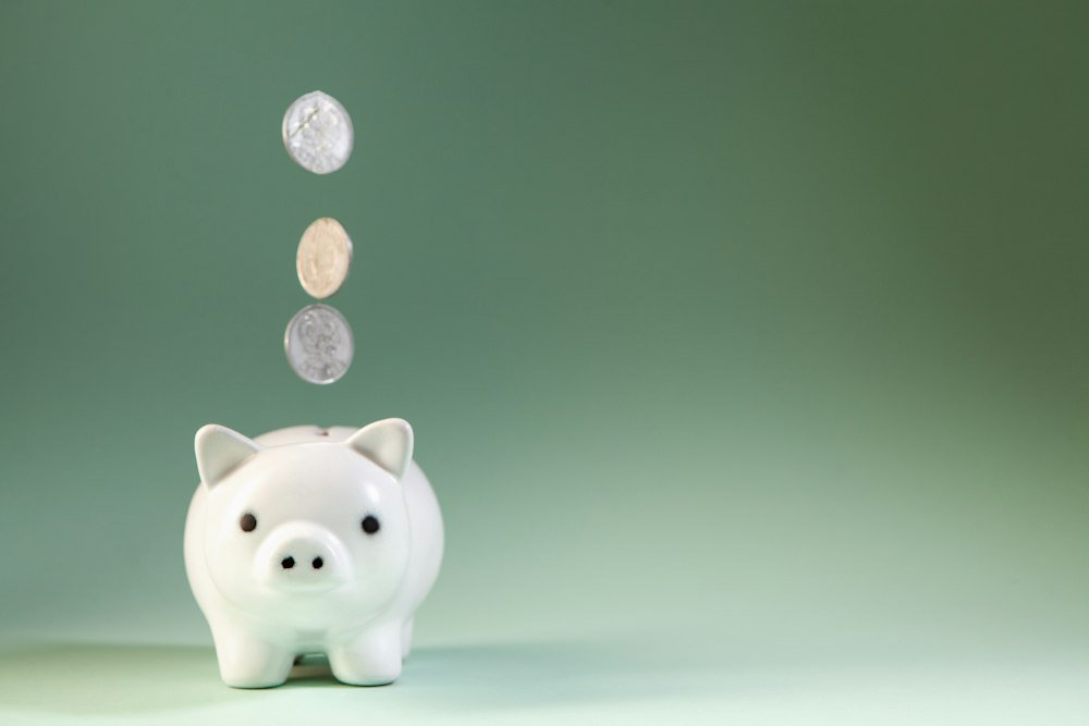 O Que É CDI e Quanto Ele Faz o Seu Dinheiro Render Hoje? Moedas caindo num cofrinho, comparação entre CDI e poupança