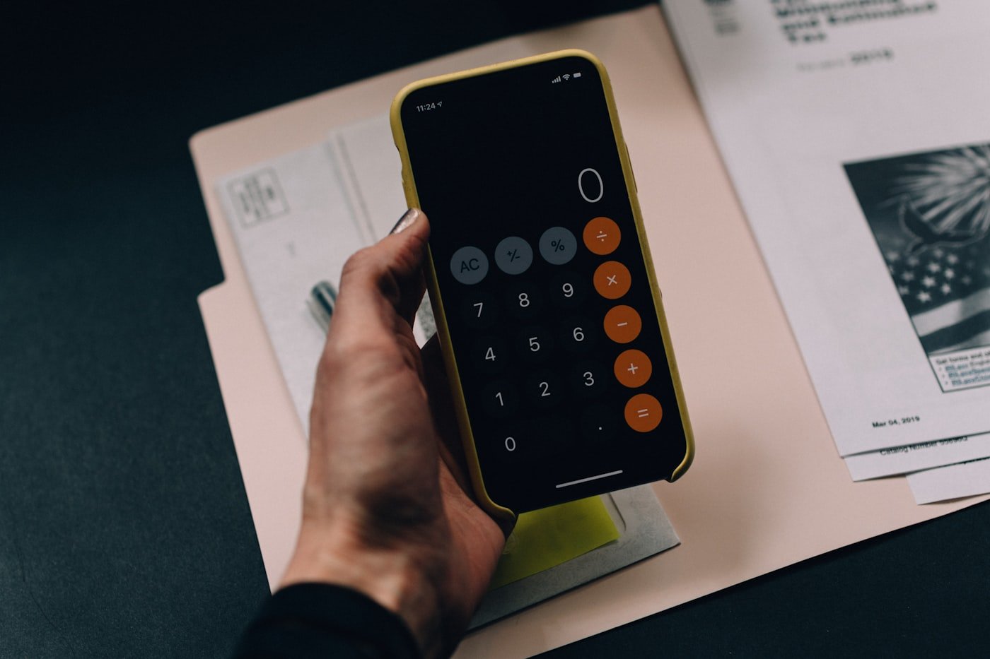 Mão segurando o celular com a previsão de gastos do mês em andamento