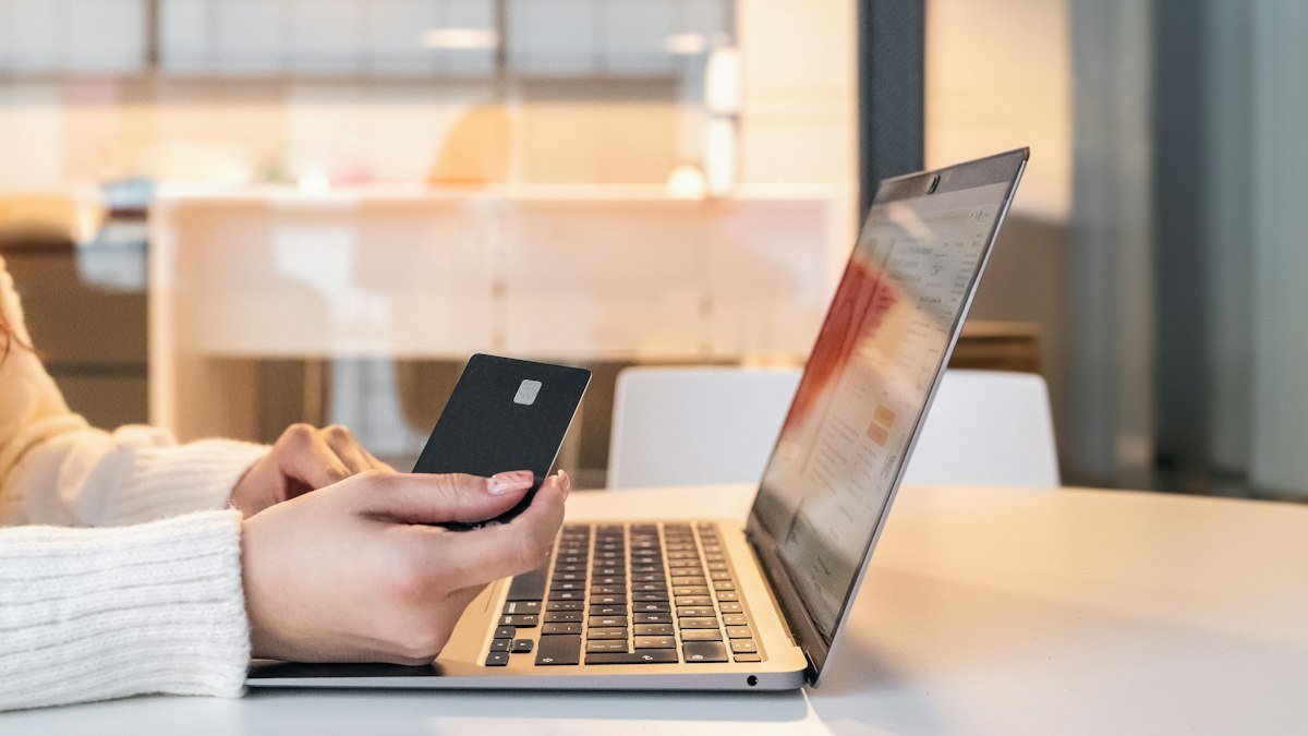 Mulher com cartão e celular diante do notebook conferindo como saber se um site é confiável antes de comprar
