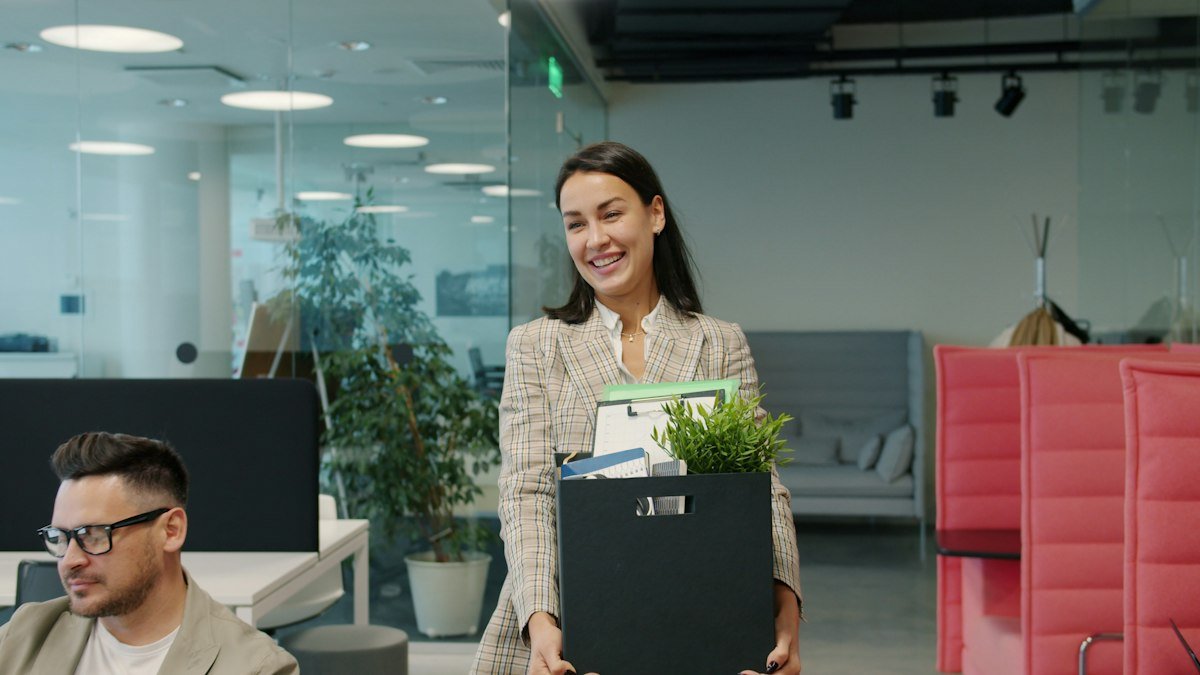 O que é aviso prévio: funcionária deixando o escritório com uma caixa de pertences no último dia de trabalho