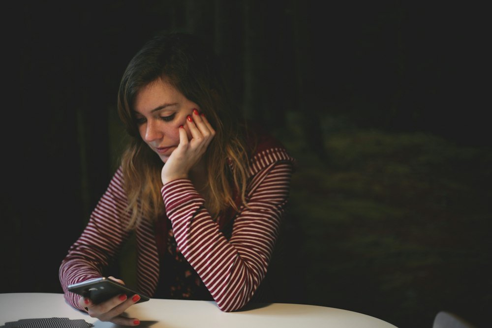 Mulher olhando o celular apoiada na mesa, ao receber mensagem pedindo devolução de Pix errado
